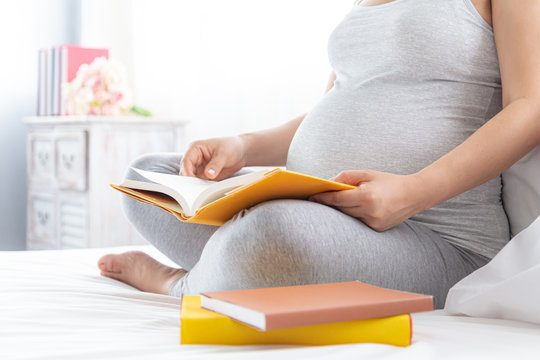 Pregnancy and motherhood concept - Happy pregnant woman reading book on white bed. - Powered by Adobe