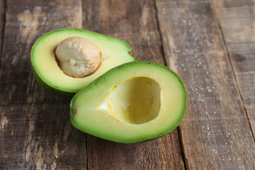  avocados one cut in two with seed, on wooden surface