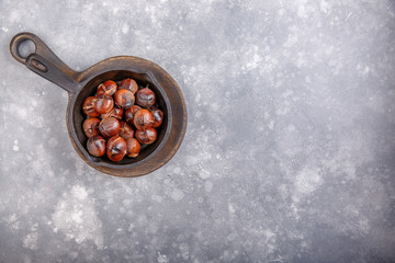 Roasted edible sweet chestnuts served in cast-iron skillet on gray background. Top view. Copy space.