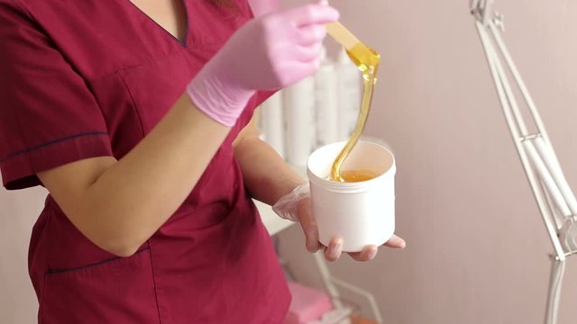 Beautician removes sugar paste for waxing with a wooden stick, preparing for the sugaring of male breast. Beautician takes sugar paste with a spatula from the banks for depilation of the male breast.