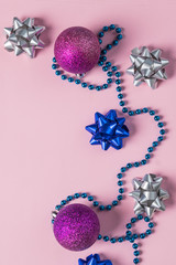 Christmas beads and ornaments on pink. New Year balls, confetti. Winter holidays preparations. Top view. Minimal festive card.silver and blue bow with decoration and sparkles. Festive concept.