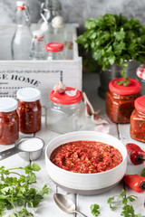 Process of cooking hot sauce of red hot peppers. Ingredients: pepper, greens, basil, paprika on a wooden table. Glass jars with ready-made sauce