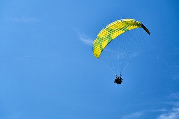 A tandem paraglider and with a yellow and blue parachute and high altitude clouds.