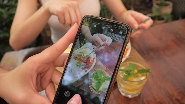 Two young women friends eat breakfast together take food photo of dishes for social media closeup touchscreen display