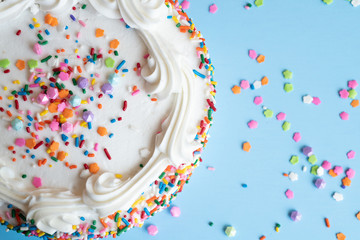 Top View of a cake with white icing and colorful sprinkles on a light blue background