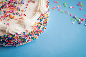 Up close side view of a cake with colorful sprinkles on a blue background