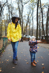 Happy mother with daughter walking in the autumn park. Baby girl pointing finger forward. Enjoying time together outdoors at weekend.