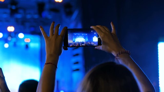 Unrecognizable woman hands silhouette taking photo or recording video of live music concert with smartphone at night. Photography, entertainment and technology concept