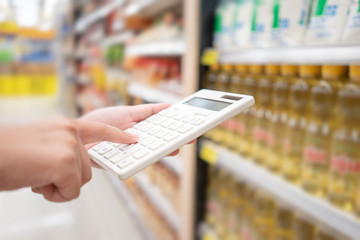 A beautiful Asian woman holding a calculator to calculate the cost and price reduction in a supermarket. Concept of price reduction, saving and value