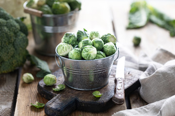 Young raw brussels sprouts in a metal cup on a wooden background.