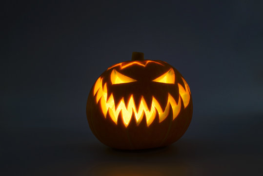 Bright orange Jack-o'-lantern pumpkin on dark solid background. Glowing eyes and a terrible grin. Halloween minimal concept. Copy space. Desktop wallpapers