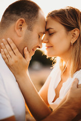 Side view close up portrait of lovely caucasian adult couple sitting face to face with closed eyes smiling against sunset.