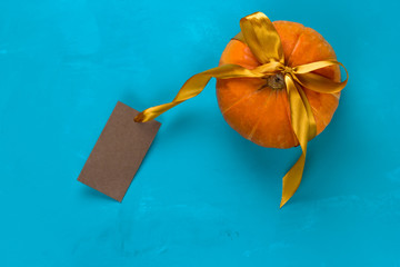 top view pumpkin decorated golden satin ribbon and mock up empty vintage paper label  on a blue background