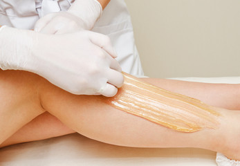 Naklejka premium Cosmetologist beautician waxing female legs in the spa center beauty salon