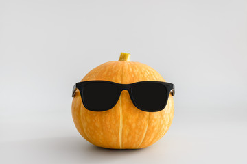 Juicy bright orange pumpkin in black sunglasses on a white solid background. Halloween minimal concept. Copy space.