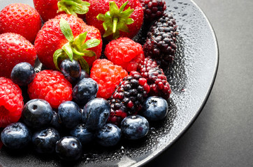 A horizontal shot of a plate of fresh summer fruit showing strawberries blue berries black berries and mulberries 