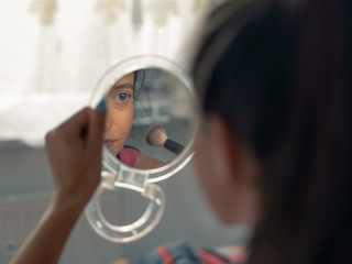 Young attractive woman looking herself in the mirror while doing her makeup