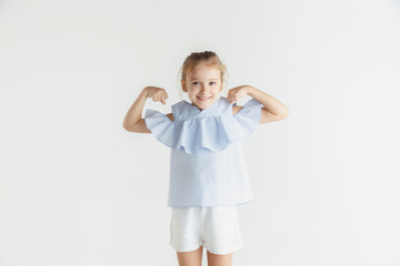 Stylish little smiling girl posing in casual clothes isolated on white studio background. Caucasian blonde female model. Human emotions, facial expression, childhood. Winning, celebrating, smiling.