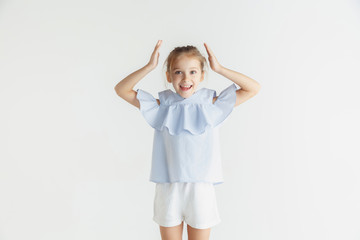 Stylish little smiling girl posing in casual clothes isolated on white studio background. Caucasian blonde female model. Human emotions, facial expression, childhood. Looks happy and amazed.