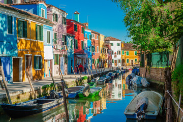 Fototapeta na wymiar Colorful vibrant houses along a green canal with old boats in Burano Italy