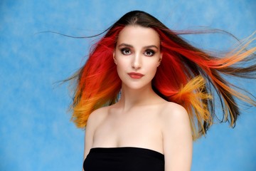 Studio portrait of a model with perfect makeup and colored hair on a blue background. Beautiful female face of a pretty girl. Perfect makeup. Skin care. Fashionable cosmetics.