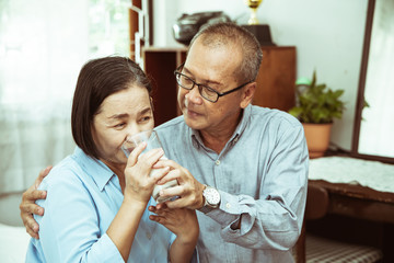 Asian  senior couple is dancing and smiling while cooking together in kitchen.
