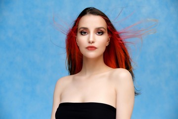 Studio portrait of a model with perfect makeup and colored hair on a blue background. Beautiful female face of a pretty girl. Perfect makeup. Skin care. Fashionable cosmetics.