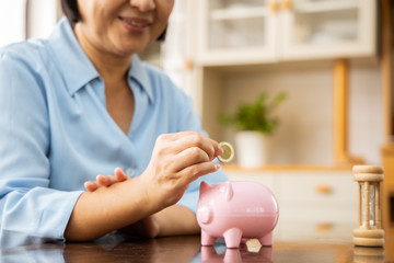 Obraz na płótnie Canvas hand putting coin money to piggy bank saving, Close up of Old Asian woman smiling putting a coin inside piggy bank as investment.
