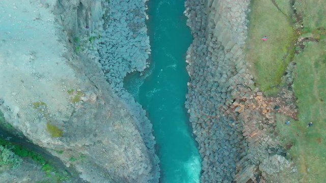 Aerial Zoom Out over Studlagil Canyon, East Iceland. Impressive landscape with Basalts Colums in  Glacier Valley, crystal clear water of Glacial River. daylight and tourists in The Valley Jökuldalur.