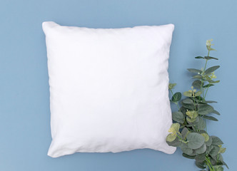 Blank white cushion mock up on blue background with eucalyptus sprig right and space left - empty and ready to add your own design 