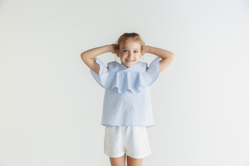 Stylish little smiling girl posing in casual clothes isolated on white studio background. Caucasian blonde female model. Human emotions, facial expression, childhood, sales. Resting and smiling.