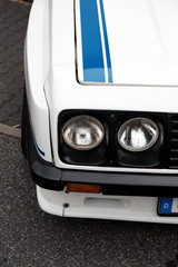 Weißer Tourenwagen mit Doppelscheinwerfer und Rallyestreifen im Stil der Siebzigerjahre für den...