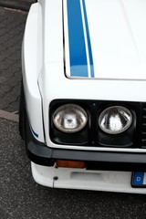 Weißer Tourenwagen mit Doppelscheinwerfer und Rallyestreifen im Stil der Siebzigerjahre für den...