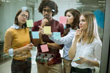 Young business people discussing in front of glass wall using post it notes and stickers