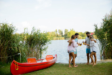 Group of friends with cider bottles standing by the boat near the beautiful lake and having fun