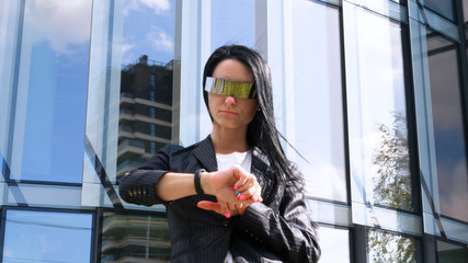 Portrait of young beautiful business woman (student) in suit, future glasses, smiling, successful looking at sides, with skyscraper background. Concept: New business, Communication, Future,  Manager.