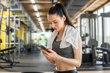 Young sportive woman using phone after training in gym