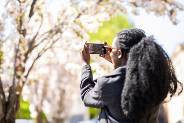 Rear view of african american tourist woman visiting a picturesque city street destination, using a smart phone taking pictures on summer holiday, outdoors. Black woman travel technology recreation.