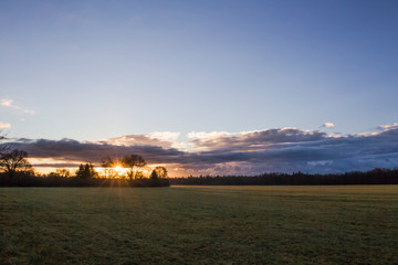 Sunrise over fields in cloudy sky