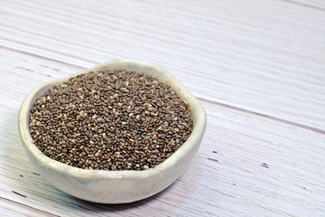 Chia seeds in little ceramic bowl on white wooden table.