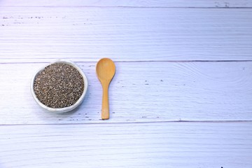 Chia seeds in little ceramic bowl and an empty wooden spoon on white wooden table with copy space.