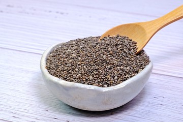 Little wooden spoon picking Chia seeds from small white ceramic bowl.