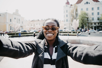 Young pretty african woman take selfie on the sunny city street