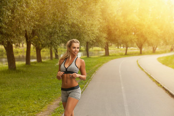 Beautiful healthy fitness blond woman in fashion sport wear running and practices yoga in the park at sunset