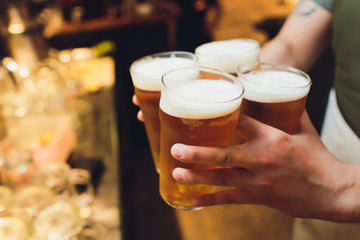 waiter holds four glasses of beer in hands in a bar or pub. Beer glasses.