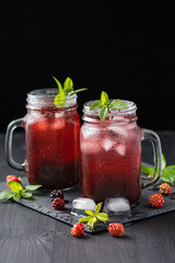 Fresh blackberry smoothie. Fresh summer cocktail with blackberry and ice cubes on a dark background on a black wooden table