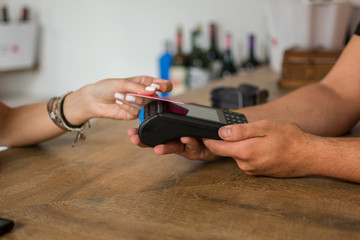 A young woman pays with credit card in a pub. The waiter holds a credit card terminal. Close up