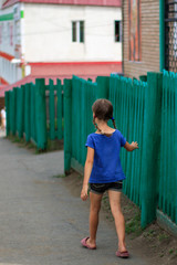 A girl walks around the city along the old fence. Travel with child