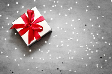 Gift box with red ribbon on grey background with star.