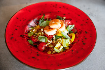 delicious and appetizing salad of shrimp, tomatoes, spinach, cheese, nuts, pate lies on a red plate in a restaurant